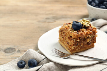 Piece of delicious layered honey cake with blueberries and nuts served on wooden table, closeup. Space for text