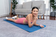 Young attractive asian woman in sportswear lying down or reclining on exercise mat. Home exercising and workout routine on the floor. Vigorous