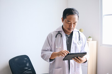 Serious Asian doctor working with digital tablet computer in modern office at hospital, tele medicine consultation.