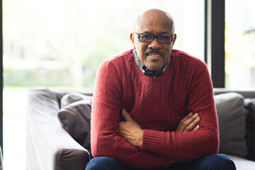 Portrait of happy senior biracial man wearing glasses sitting on sofa at home