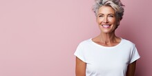 Beautiful mature woman in her fifties with pink background, smiling senior lady in a white t-shirt, studio shot with copy space