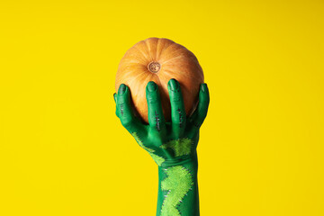 Pumpkin in green female hand on yellow background, close up