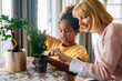 Happy caucasian mother and her adopted african american daughter taking care of plants indoors.