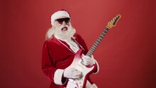 Medium Shot Of Santa Claus In Red Costume, With Beard, Sunglasses And Silver Chain, Playing Electric Guitar, Rocking, Singing And Sticking Out Tongue, On Red Background. Template, Copy Space