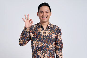 Wall Mural - Smiling young Asian teacher man wearing batik shirt doing ok sign with fingers isolated on white background