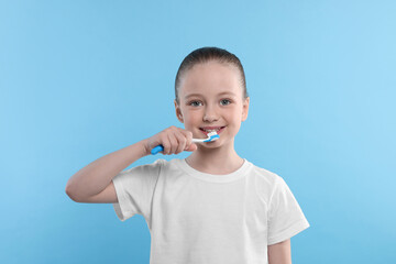 Wall Mural - Happy girl brushing her teeth with toothbrush on light blue background