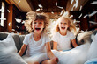 Dos niños entusiasmados felices y risueños se divierten en el interior de casa en una fiesta familiar con cogines en el sofá.