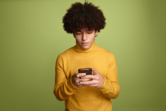 Focused Hispanic man using smartphone near green background
