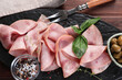 Tasty ham with basil, olives, sea salt, peppercorns and carving fork on wooden table, top view