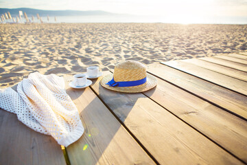 a hat, a cape and two cups of coffee stand on a pier near the sea