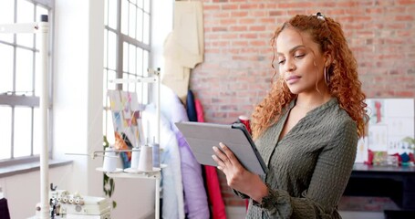 Wall Mural - thoughtful biracial female fashion designer using tablet at studio, slow motion