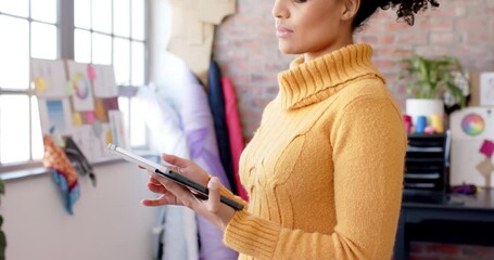 Wall Mural - happy biracial female fashion designer using tablet at studio and smiling, slow motion