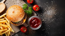 Fresh Homemade Burger With Black Sesame Seeds In White Plate With French Fries Potatoes, Served With Ketchup Sauce In Glass Jar Over Gray Wooden Surface. Top View