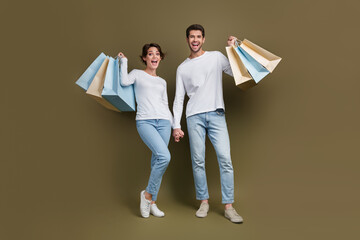 Full length photo of excited funky married couple wear white shirts rising bargains isolated brown color background