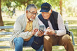 © aLListar/peopleimages.com - Elderly men, friends and phone in park, reading and army memory with thinking, relax and sunshine. Senior military veteran, smartphone social media and talk on bench, nostalgia and remember service