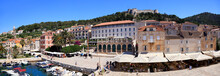 Panoramic View Of Hvar, Including The Fortress On The Hill And Shops, Restaurants And Harbor On The Foreground, Croatia