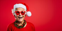 Studio Portrait Of Eccentric Elderly Grandma With Holiday Spirit, Dressed Up In Christmas Outfit With Wreath, Ornaments, And Santa Hat