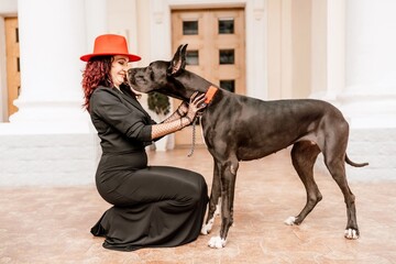 A photo of a woman and her Great Dane walking through a town, taking in the sights and sounds of the urban environment.