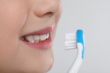 Wall Mural - Girl brushing her teeth with toothbrush on light grey background, closeup