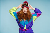 Smiling girl wearing stylish ski overalls, ski goggles, looking at camera. Winter travel concept