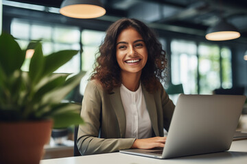 Portrait of beautiful female employee, IT specialist, in a modern office, happily working on laptop as a programmer for a startup company.