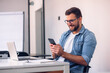 © kerkezz - Young attractive man using mobile phone while working on laptop in his office.