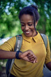 © kerkezz - Happy young woman with backpack on city break. A woman is standing in the park and looking at her watch.