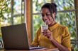 © kerkezz - Beautiful young woman working on a laptop while drinking coffee on a beautiful porch surrounded by greenery.