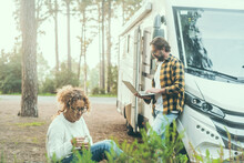 Travel Couple Adult People Man And Woman Enjoy Outdoor Leisure Activity Outside A Modern Rv Vehicle Camper Van Parking In The Forest. Adventure Traveler Vanlife Lifestyle. Digital Nomad Using Computer