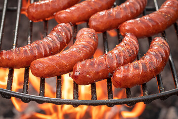 Wall Mural - Grilled sausages seasoning with spicy spices on grill with fire.