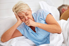 Couple, coughing or sick old woman in bed with husband or man with flu virus, tuberculosis or health problem. Chest pain, mature lady or senior person with cold, fever or lung illness in home bedroom