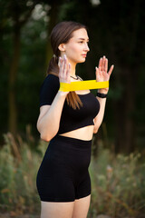 Young woman working out with fitness rubber bands in the forest, girl training hands on nature, sport concept