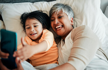 Canvas Print - Selfie, smile and old woman with child on bed bonding, relax and love for happy family with care. Photography, technology and grandmother with little girl in bedroom on video call together in home