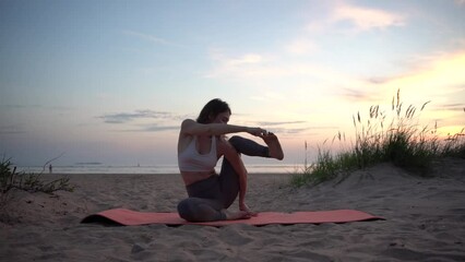 Wall Mural - A young woman instructor flexible slender body yoga asana pose training, uses a mat for exercises against the background of sunset.  Mental health and a healthy lifestyle.