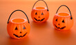 Halloween jack-o-lantern candy buckets or pail on orange background