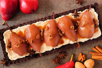Poster - Spice poached pear tart with caramel on a chocolate and cream base. Overhead view table scene on a dark stone background.