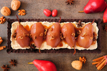 Poster - Spice poached pear tart with caramel on a chocolate and cream base. Above view table scene over a dark stone background.