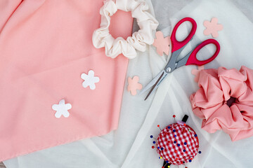 two pink and white scrunchies, pincushion and sharp red scissors on thin white and pink fabric. Hair accessories