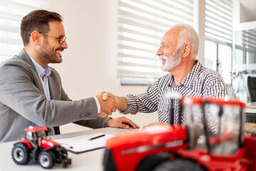 Investment in agricultural machinery and farming equipment. Farmer and dealer shaking hands and signing contract.