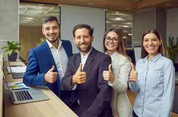 Group of business people men and women looking at camera, showing thumbs up sign and smiling. Company employees team or a group of staff standing in office confidently and cheerfully on workplace.