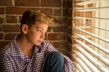 Warm Natural Light Portrait Of A Boy With Freckles Sitting Looking Out Of A Window