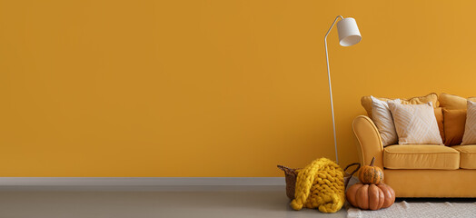 Interior of bright living room with stylish sofa, standard lamp and pumpkins near yellow wall. Banner for design