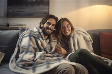 young couple of boy and girl smiling sitting on the sofa at home wrapped in a blanket