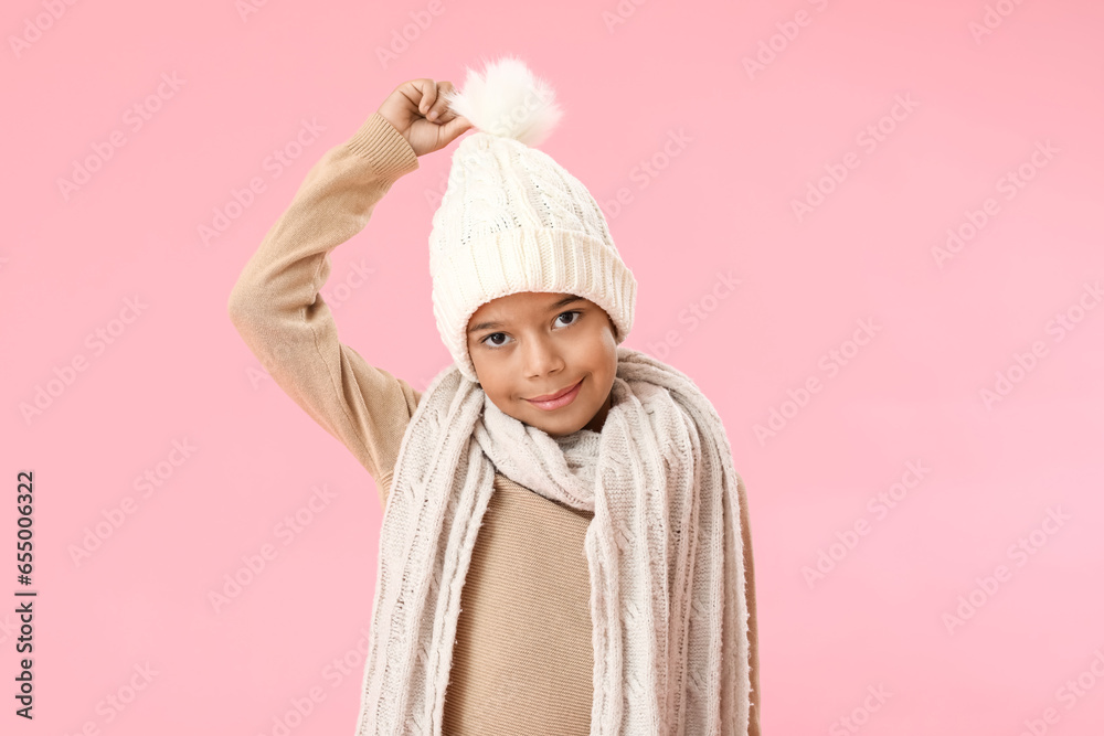 Cute African-American boy in warm winter clothes on pink background