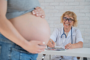 Doctor obstetrician gynecologist at his desk in the background. Close-up of a pregnant woman's belly.