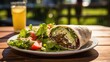 A lole shot showcases the felafel wrap in an outdoor setting, basking in natural light. The wrap is nestled on a wooden table, adorned with a side of crisp, golden fries and a refreshing