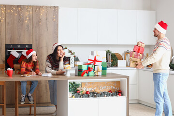 Poster - Little girl with her mother receiving Christmas gifts in kitchen