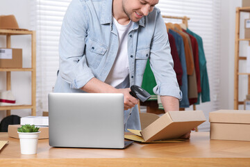 Canvas Print - Seller with scanner reading parcel barcode at table in office, closeup. Online store