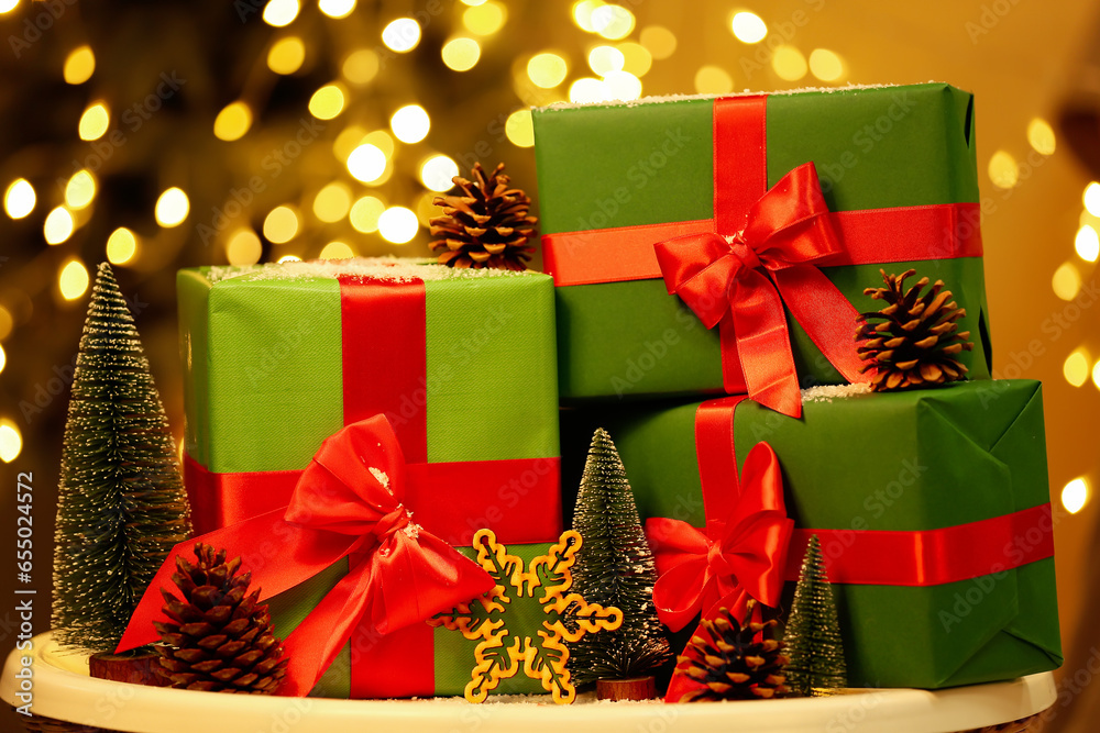 Christmas gift boxes with fir trees and pine cones on table against blurred lights, closeup