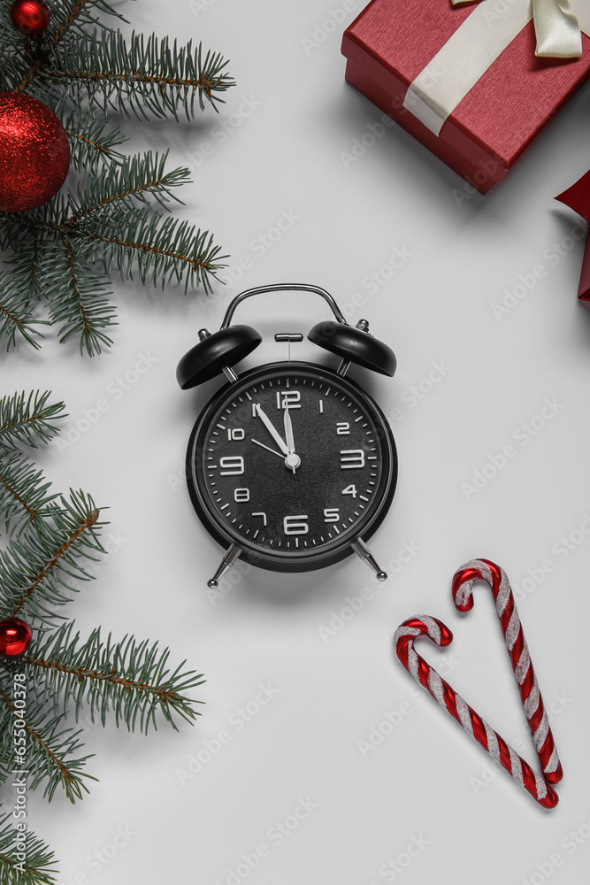 Alarm clock with Christmas tree branches and candy canes on white background